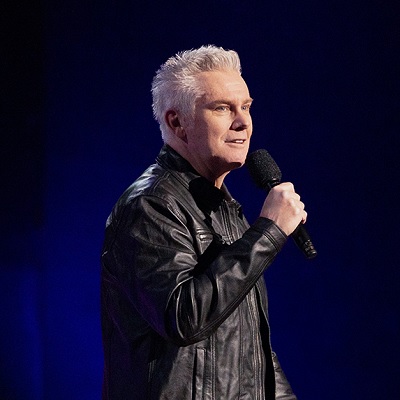 Brian Regan holding a mic on stage